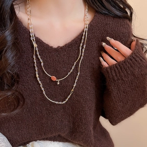 Detail of layered gold beaded necklace with oval pendants on a brown sweater