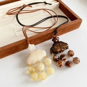 Detail of cloud-shaped resin pendants with bead tassels and suede cord on a jewelry box