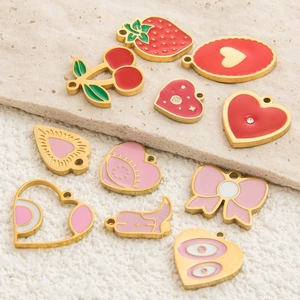 Flat lay of colorful enamel fruit and heart charms in gold finish on white stone surface