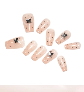 Detail of nude cat-eye press-on nails with white dots and 3D silver butterfly charms