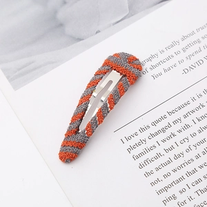 Detail of handmade knit metal hair clip with orange and gray yarn texture on white card