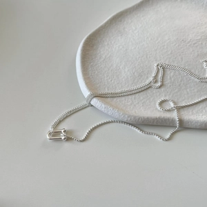 Close-up of minimalist 925 sterling silver U-buckle necklace on a white ceramic plate