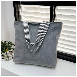 Detail of grey canvas tote bag featuring dual black and white striped webbing handles