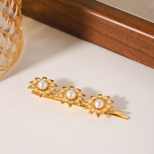 Golden hair clip featuring three daisy flowers with pearls on a marble surface