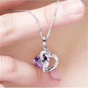 Close-up of a heart-shaped necklace featuring a purple gemstone and sparkling crystals