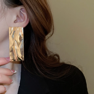 Detail view of gold rectangle earrings with unique hammered metal texture on a model