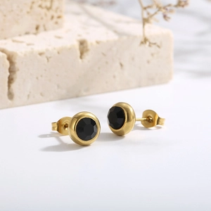 Detail shot of gold stud earrings with faceted black gemstone on a natural stone base