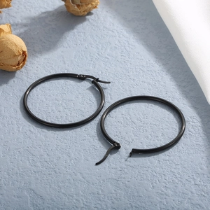 Detail of large black stainless steel hoop earrings on light blue textured background