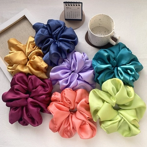 Flat lay of colorful oversized satin scrunchies in navy, gold, and purple on white fabric