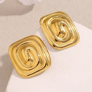 Gros plan de boucles d'oreilles carrées labyrinthe en acier doré sur pierre blanche
