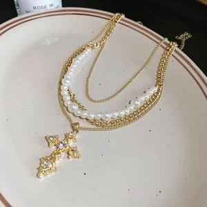Detail of a gold layered necklace with white pearls and a baroque diamond cross pendant