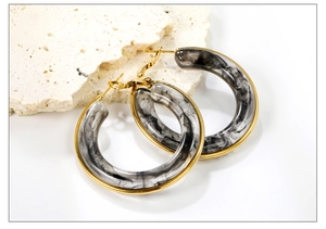 Detail view of large C-shaped resin earrings with black and white marble pattern and gold trim