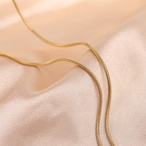Detailed macro view of a gold-toned sleek snake chain necklace on peach satin fabric