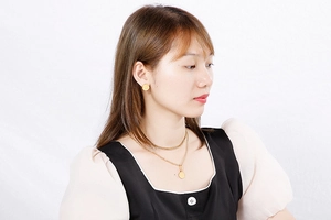 Detail showing a double-layered gold necklace and matching round stud earrings on a model