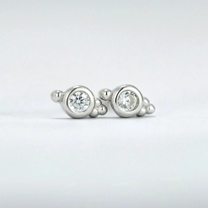 Macro shot of silver stud earring featuring a round clear zircon and metal bead details