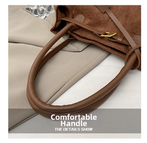 Detail view of the brown leather tote bag handle and gold square buckle attachment
