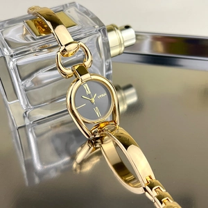 Close-up of gold metal bracelet watch with black dial and Roman numerals on reflective surface