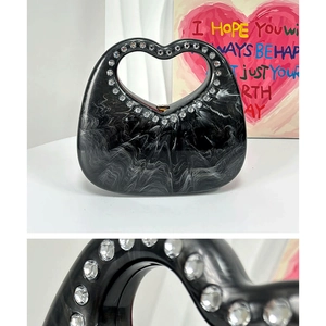 Macro shot of rhinestone heart-shaped handle on black marble acrylic clutch bag