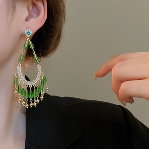 Détail de boucles d'oreilles pendantes dorées avec perles gouttes vertes et fleur bleue