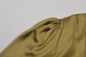 Dettaglio ravvicinato del design a pieghe sulla spalla di un abito in raso verde oliva
