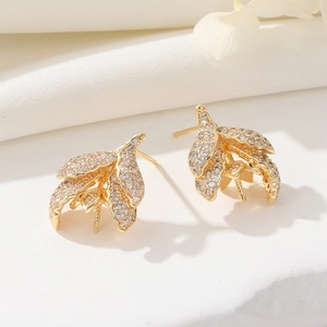 Detailed view of gold-plated leaf earrings with shimmering pavé zircon on silk fabric