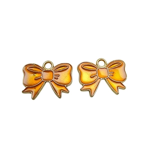 Close-up of orange enamel bow pendants with gold metal borders for DIY jewelry making