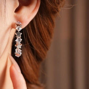 Detail of silver star C-shaped earrings with clear zircon stones on a model's ear