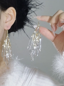 Detail of long gold earrings featuring multi-layered crystal acrylic water drop pendants