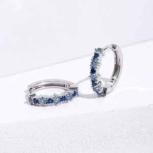 Silver hinged hoop earrings with square blue zircon stones on a white background