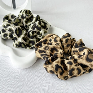 Close-up of leopard print satin scrunchies in green and brown on a ceramic tray