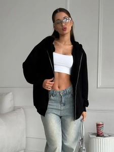 Detail view of a black oversized zip-up hoodie paired with light blue straight jeans