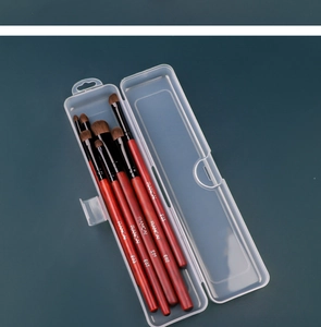 Five professional makeup brushes with red wooden handles in a clear storage box case