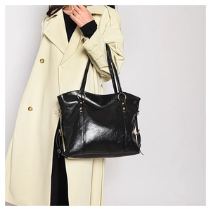 Glossy black tote bag with gold hardware worn by a model in a beige coat side view