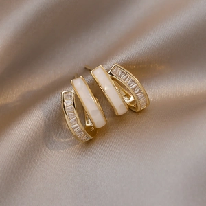 Detail of gold-plated earrings with white enamel and sparkling zircon on silk