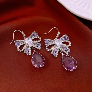 Close-up of bow-knot earrings with purple teardrop crystals on red silk fabric