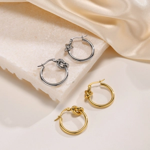 French style knotted hoop earrings in gold and silver finish set on white marble
