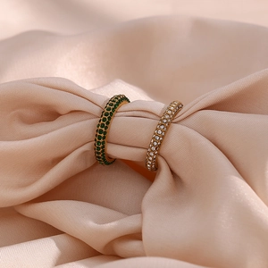Close-up of gold rings with green and clear zircon stones on soft pink silk fabric