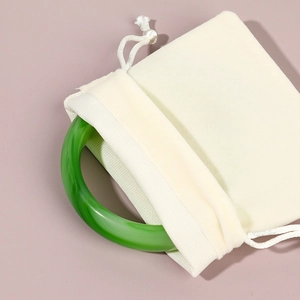 Green jade bangle partially tucked in a beige velvet drawstring jewelry pouch