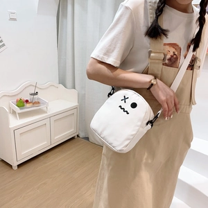 Détail du sac bandoulière en toile blanche avec broderie cartoon sur la sangle