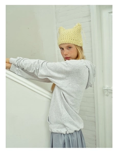 Close-up of a yellow knitted hat with cat ear design and bow detail paired with a grey hoodie