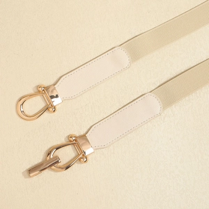 Detail of elegant beige elastic waist belt featuring golden equestrian stirrup buckle