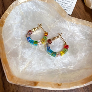 Detail of colorful crystal beaded gold hoop earrings resting on a heart shell tray