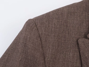 Gros plan détaillé du tissu texturé en laine marron sur l'épaule et le revers du blazer