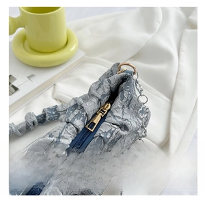 Detail of blue pleated fabric bag with gold zipper and floral chain strap accessory