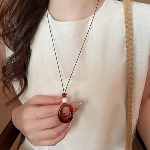 Détail du collier avec pendentif en résine ambrée et perle crème porté par un mannequin