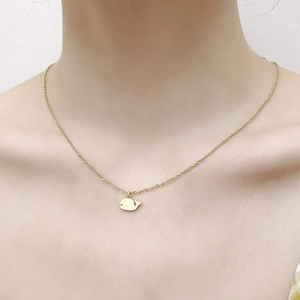 Detailed close-up of a minimalist golden whale pendant necklace worn on a woman's neck