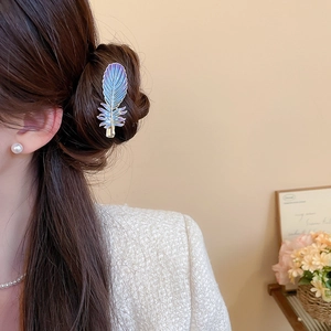 Détail d'une pince à cheveux plume colorée sur cheveux bruns avec bijoux en perles