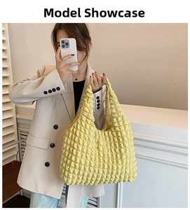 Mirror selfie showing a yellow pleated cloud handbag styled with a beige blazer