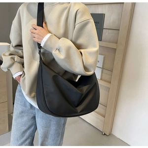 Detail of minimalist black nylon crescent crossbody bag worn by a model in casual setting