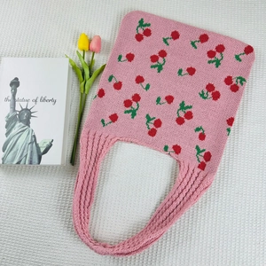 Detail of pink knitted tote bag with red cherry pattern and woven handle on grid fabric